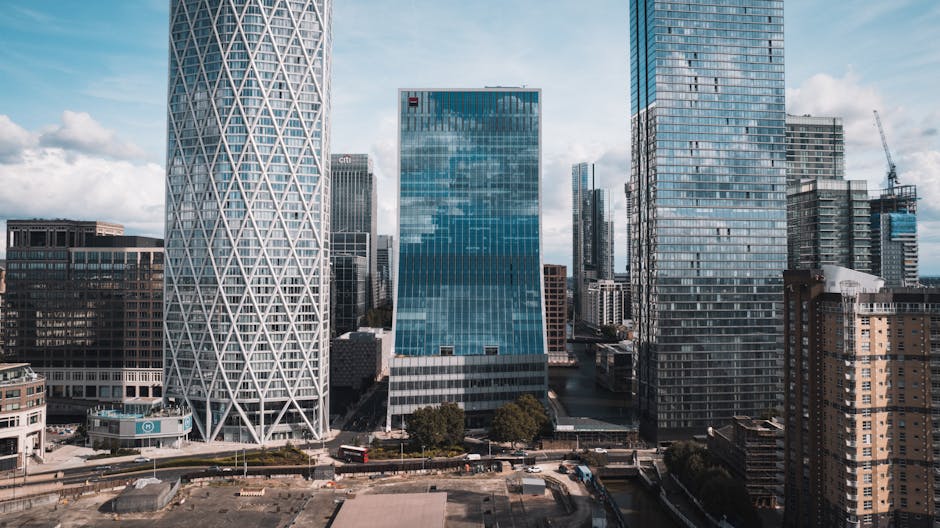 A cluster of modern high-rise office buildings in an urban setting, with the tallest building centrally positioned, featuring a grid-like pattern of windows on its facade. To the left is a slightly sh